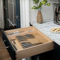 an open drawer in a kitchen with utensils on the counter and flowers in a vase