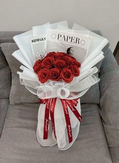 a bouquet of red roses sitting on top of a gray couch next to a magazine