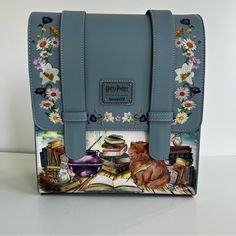 a blue purse with an image of a cat and books on the front, sitting on a table