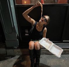 a woman sitting on the ground holding a plastic container with food in it and wearing knee high boots