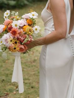 a woman in a white dress holding a bouquet of colorful flowers on her wedding day