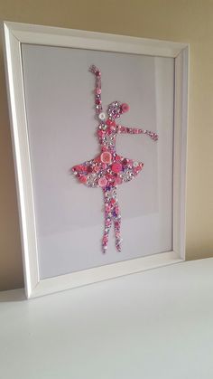 a white frame holding a pink and purple ballerina ornament in it's center