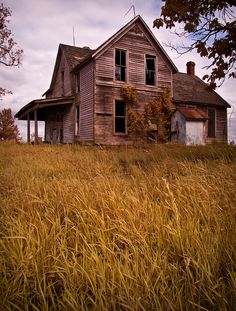 an old house sitting in the middle of a field with tall grass and trees around it