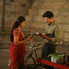 a man and woman standing next to each other in front of a bike with food on it