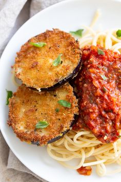 two fried eggplant patties and spaghetti on a white plate with garnish