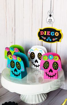 three sugar skulls sitting on top of a white cake plate next to a sign that says diego