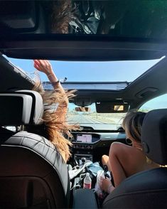 two people in the back seat of a car with their hands up to the sky