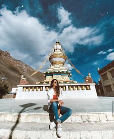 a woman is sitting on the steps in front of a building with a sky background