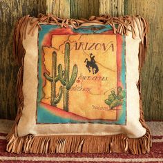 a decorative pillow with the name arizona on it and a cactus in the middle, sitting against a wooden wall