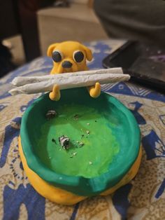 a yellow and green bowl with a stick sticking out of it's mouth sitting on top of a table