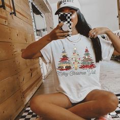 a woman sitting on the floor taking a selfie with her cell phone while wearing a hat