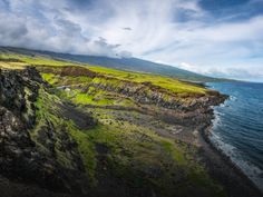 an aerial view of the ocean and rocky coastline with green grass growing on the cliffs