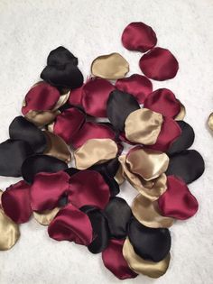 red, black and gold satin flower petals are scattered on the white surface next to each other