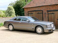 a silver car parked in front of a brick building next to a wooden garage door