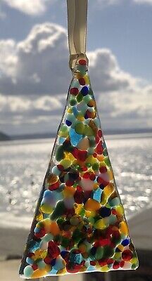 a glass ornament hanging from a hook on a beach with the ocean in the background