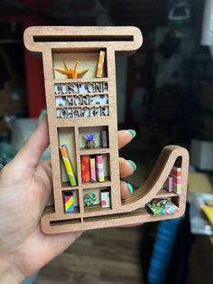 a person holding up a miniature book shelf with magnets on it's sides