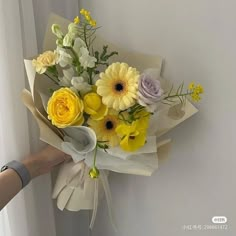 a bouquet of yellow and white flowers is being held by a woman's hand