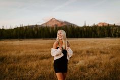 a woman in a black and white dress standing in a field with mountains in the background