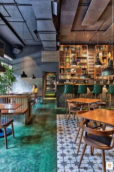 an empty restaurant with wooden tables and green chairs, in the middle of a tiled floor