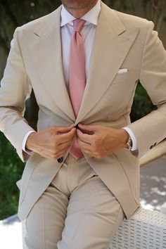 a man in a tan suit and pink tie is holding his hands on his lapel