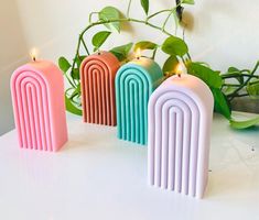 three different colored candles sitting next to each other on a white table with greenery