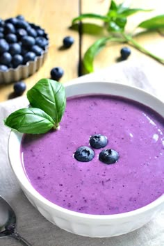 a bowl filled with blueberry smoothie and topped with fresh basil leaves