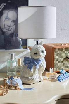 a white cat figurine sitting on top of a table next to a lamp