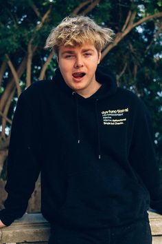 a young man with blonde hair wearing a black hoodie and making a surprised face