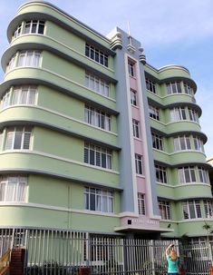 a woman standing in front of a green building with white windows and balconies