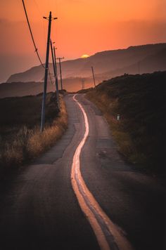 the sun is setting on an empty road with power lines and telephone poles in the foreground