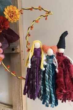 three dolls are hanging from a branch with flowers in the background and one is wearing a witches hat