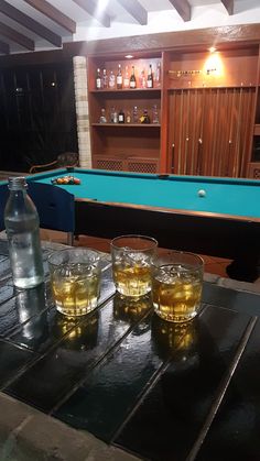 three glasses and a bottle sitting on a table with a pool table in the background