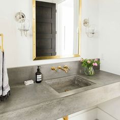 a bathroom sink sitting under a large mirror next to a vase with flowers on it