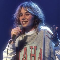 a woman with long hair holding a microphone in front of her face and making the peace sign