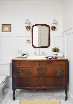 a bathroom with a sink, mirror and wooden dresser in the middle of the room