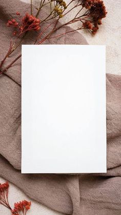 a sheet of white paper sitting on top of a bed next to dried red flowers