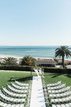 an outdoor ceremony set up with white chairs and palm trees in front of the ocean