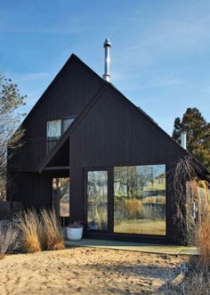 a small black house sitting on top of a dry grass covered field next to trees