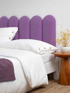 a white bed with purple headboard and pillows next to a small table on the floor