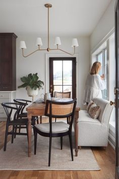 a woman standing in front of a dining room table with chairs and a bench next to it