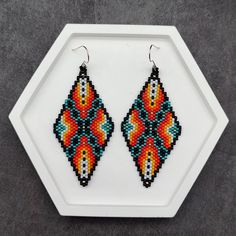 These striking geometric earrings feature a captivating gradient from red to yellow, accented by a central black and turquoise X-shaped pattern. The design combines vibrant colors with intricate beadwork, making them an eye-catching accessory for any occasion. Whether you're adding a pop of color to your daily outfit or complementing a boho-inspired look, these earrings offer a perfect blend of style and uniqueness. Created with meticulous attention to detail, these earrings are ideal for those Southwestern Multicolor Earrings With Colorful Beads, Southwestern Black Beaded Earrings For Gift, Southwestern Style Multicolor Drop Earrings, Bohemian Geometric Beaded Earrings As Gift, Handmade Southwestern Multicolor Earrings, Southwestern Multicolor Round Bead Earrings, Southwestern Style Black Earrings With Colorful Beads, Multicolor Bohemian Beaded Rectangular Earrings, Multicolor Southwestern Style Drop Earrings