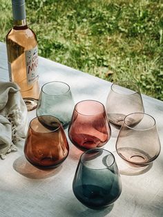 several different colored wine glasses sitting on a table next to a bottle of wine and cloth