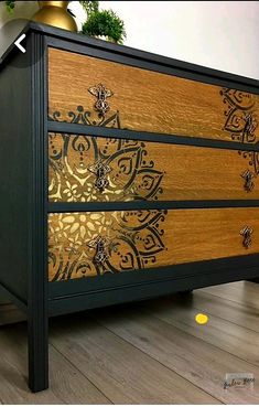 a black and gold dresser sitting on top of a hard wood floor next to a potted plant