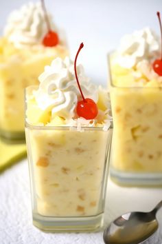 three desserts with whipped cream and cherries in small glass dishes on a table