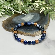 Experience the essence of harmony with the artisan-made Sodalite and Palm Wood Unisex Bracelet. This captivating accessory unites the tranquil allure of Sodalite and the rustic charm of Palm Wood, creating a wearable masterpiece that resonates with both elegance and earthy energy. Centered around the serene Sodalite beads, the bracelet showcases a palette of deep blues interwoven with delicate patterns, reminiscent of the vast expanse of a starlit sky. Sodalite is renowned for its ability to fos Blue Bohemian Bracelets For Meditation, Bohemian Blue Bracelets For Meditation, Adjustable Blue Earthy Jewelry, Nature-inspired Beaded Bracelets For Healing, Artisan Blue Bracelet As Gift, Rustic Gemstone Beaded Bracelets As Gift, Artisan Blue Bracelet For Gift, Artisan Blue Bracelet Perfect For Gift, Rustic Beaded Bracelets With Gemstone Beads For Gifts