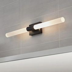 a bathroom light with two lights on the wall and tiled walls in the back ground