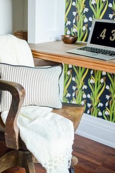 a laptop computer sitting on top of a wooden desk next to a wallpapered wall