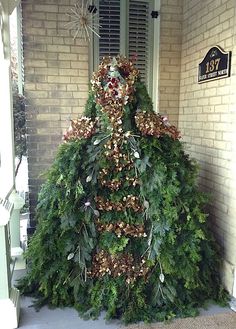 a very tall christmas tree sitting in front of a house with wreaths on it