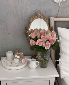 a white dresser topped with a vase filled with pink flowers next to a mirror and cup