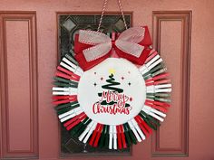 a christmas wreath hanging on a door with red and green ribbons around it that says merry christmas